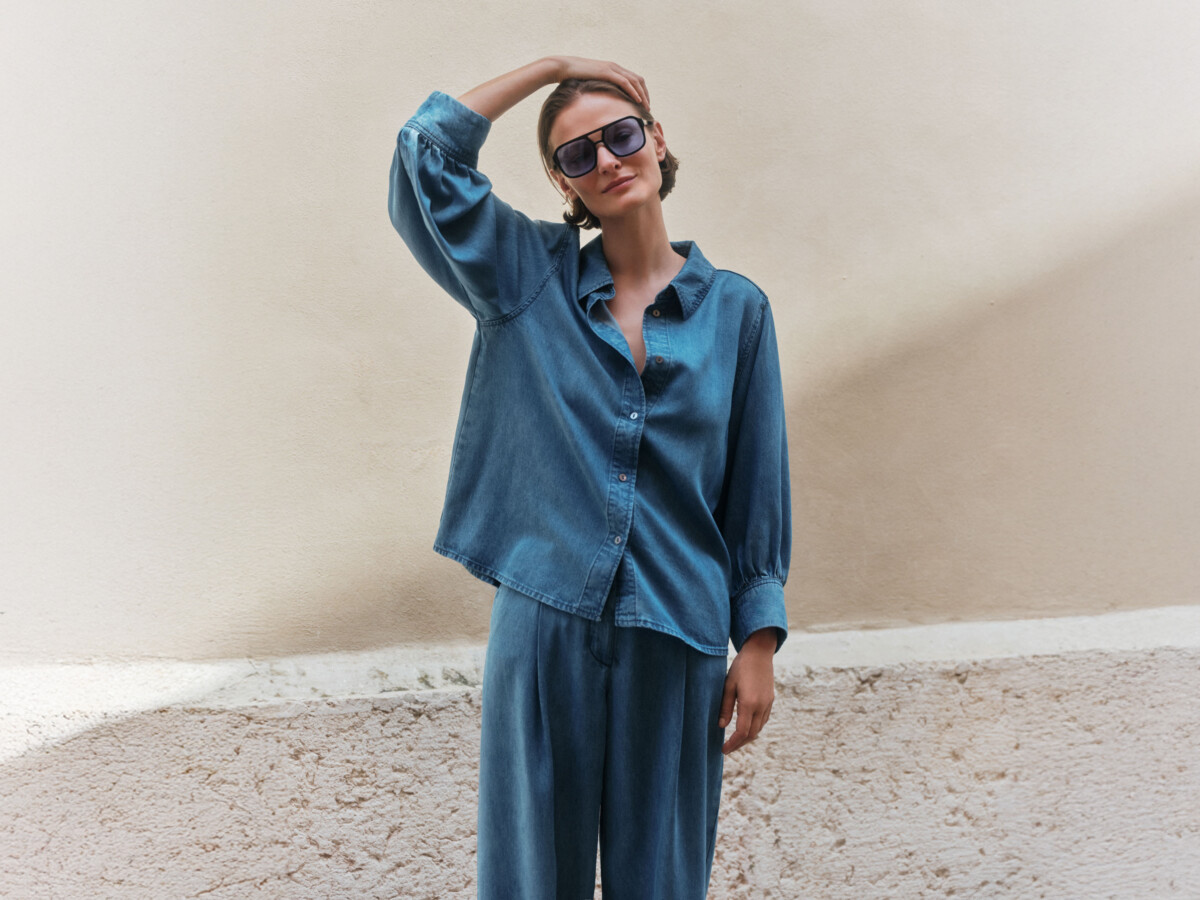 Lanius: Frau mit Sonnenbrille trägt lässiges Denim-Set aus weiter Jeansbluse und locker fallender Hose vor beiger Wand – minimalistischer Streetstyle-Look in Blau