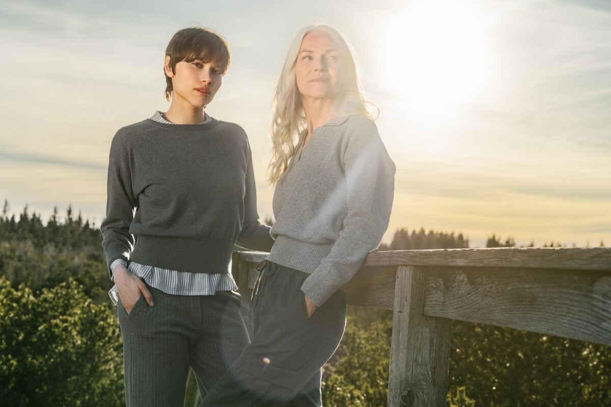 LIVING CRAFTS: Zwei weiblich aussehende Personen tragen bequeme Unisex-Wollpullover, hochwertige Strick-Sweathosen aus Wolle und Nadelstreifenhosen im Freien bei Sonnenuntergang.