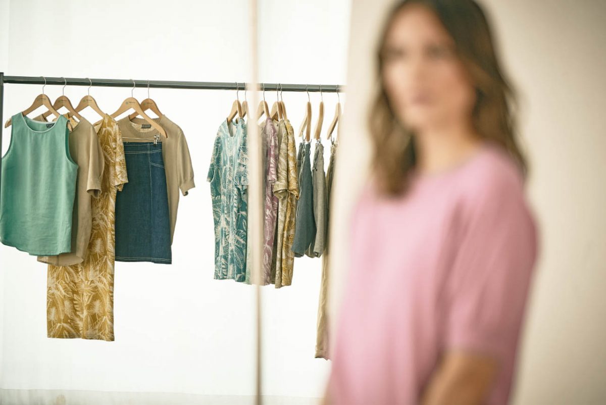 Hempage, eine Frau im rosa Oberteil ist unscharf zusehen, im Hintergrund ist Kleidung an einer Kleiderstange zusehen, Womenswear