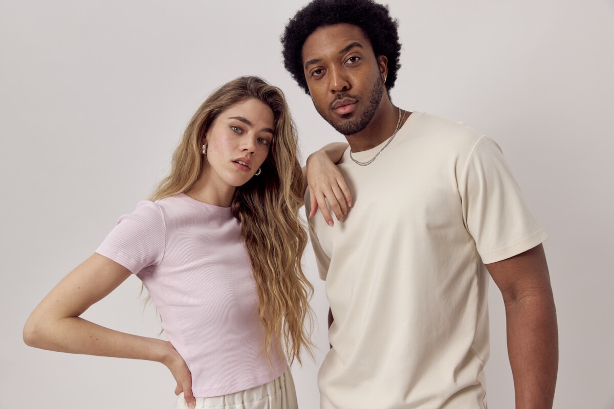 Junges Paar posiert gemeinsam im minimalistischen Studio – Frau im pastellrosa T-Shirt und Mann im beigen Crew-Neck-T-Shirt, modernes Casual-Fashion-Porträt.