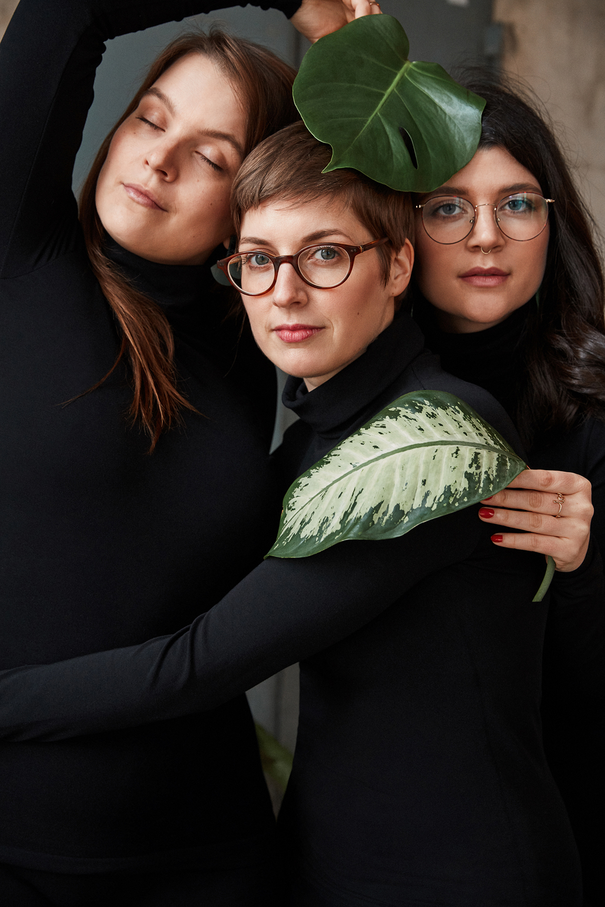 Drei Frauen in schwarzen Rollkragenpullovern von Wolford umarmen sich und halten grüne Blätter