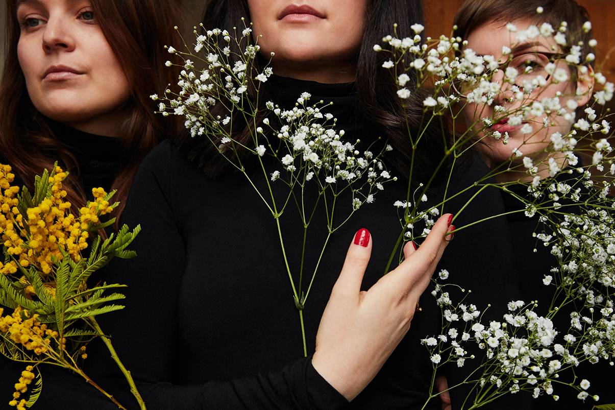 3 Frauen tragen schwarze Rollkragenpullover von Wolford und halten gelb-weiße Blumen vor ihre Gesichter