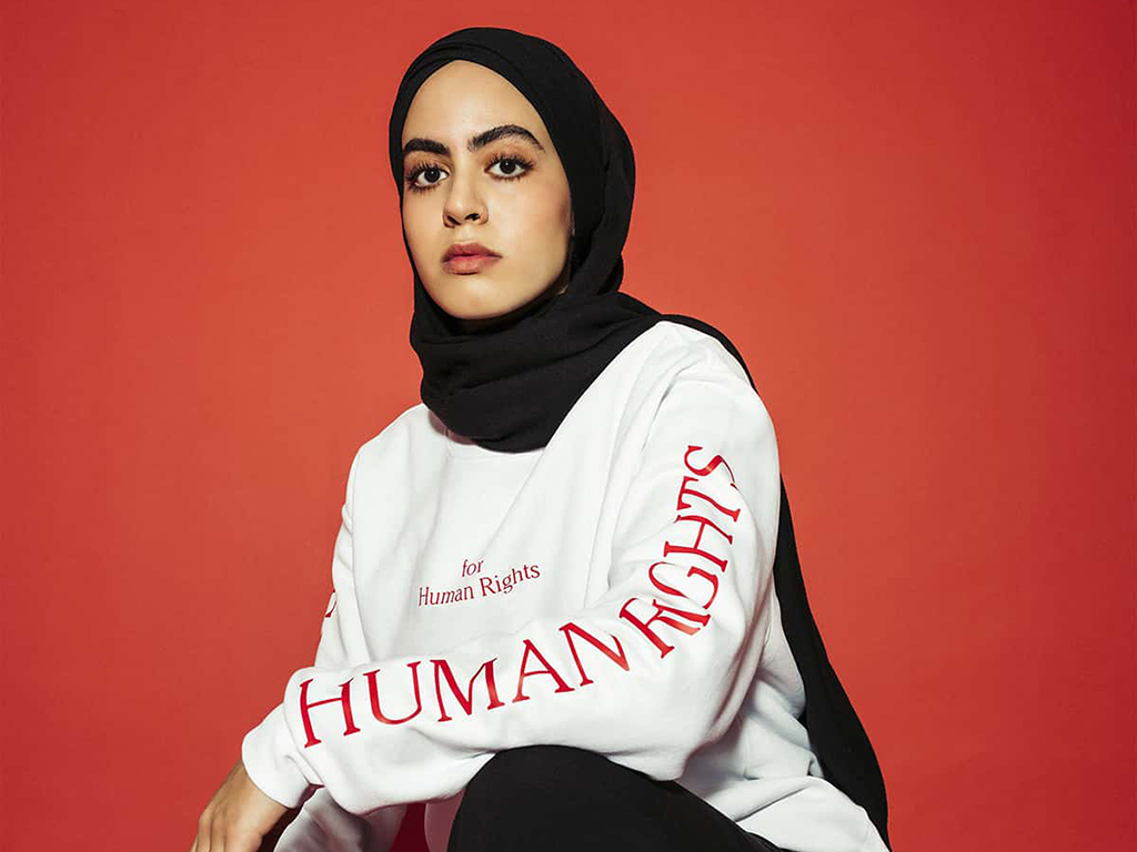 For Human Rights, eine Frau mit Kopftuch trägt das Human Rights Langarm T-Shirt vor einem roten Hintergrund, Womenswear Menswear