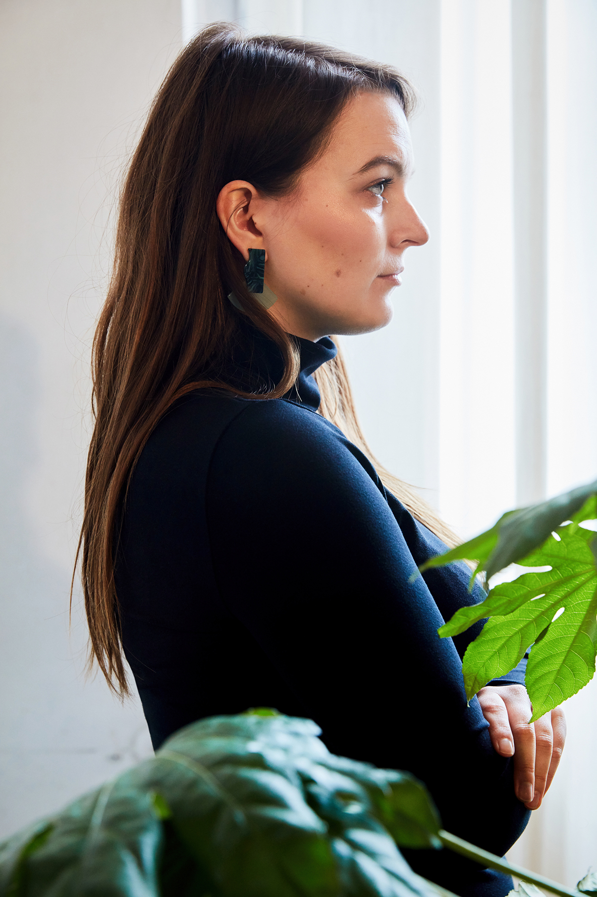 Profil von Frau mit langen Haaren und schwarzem Rollkragenpullover von Wolford, weißer Hintergrund mit Pflanzen