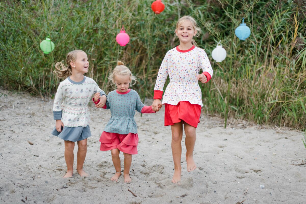 Drei Kinder laufen durch Sand und tragen blaue, weiße und rote Kleider der Chleiderei