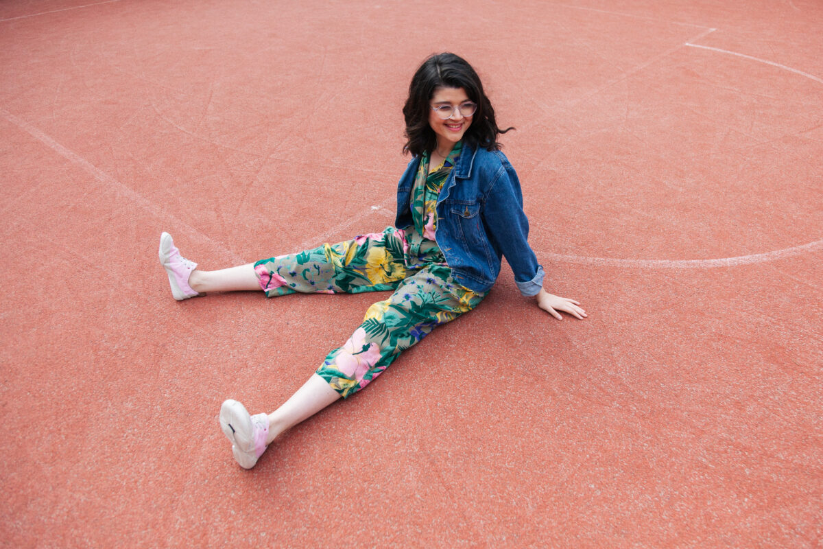 Person sitzt mit weit geöffneten Beinen auf einem Sportplatz und lacht