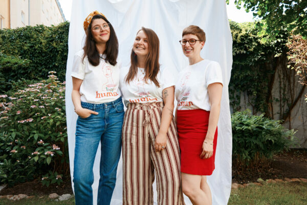 Jana, Nina und Vreni stehen vor einem weißen Tuch in einem Garten, sie tragen alle das Human-Shirt.