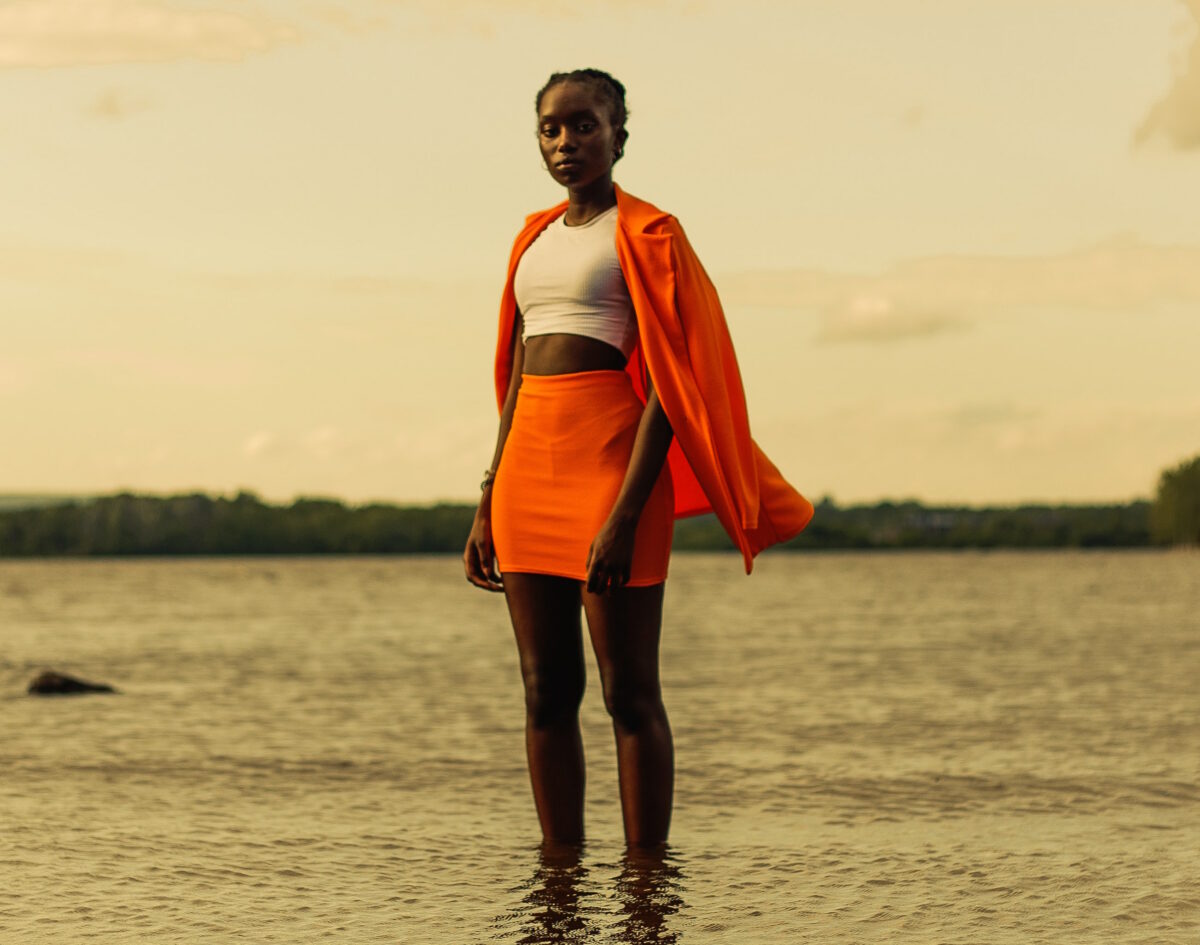 Eine Person steht im Wasser und trägt einen orangefarbenen Rock, orangefarbenen Blazer und weißes Crop-Top