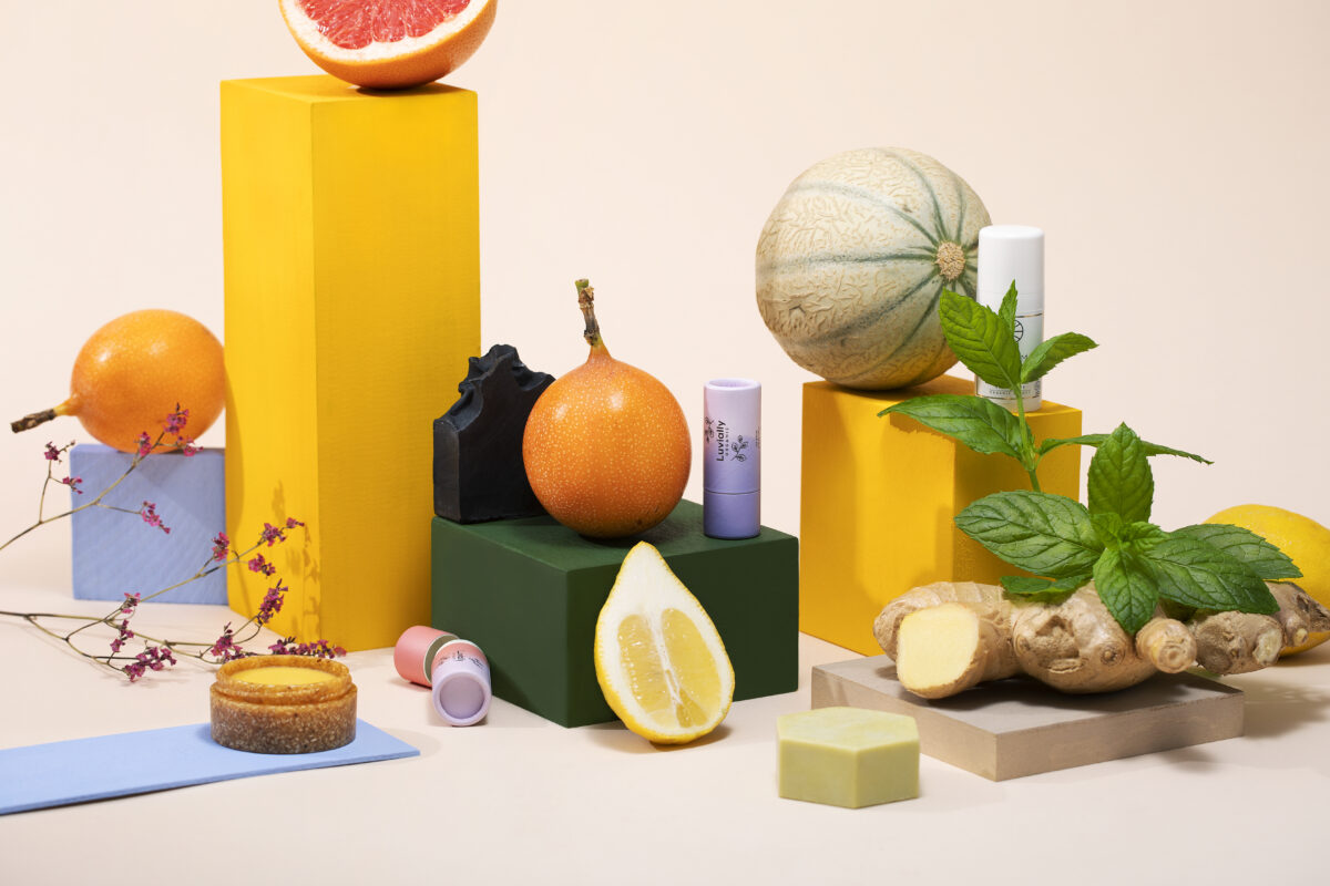 Vor einem neutralen Hintergrund sind verschiedene Beautyprodukte und aufgeschnittenes Obst, verteilt Zwischen verschiedenfarbigen Klötzen.