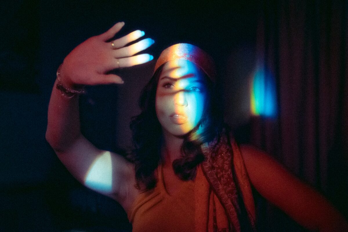 Eine Person wird vom Licht, das in Regenbogenfarben spiegelt, geblendet und hält die Hand vors Gesicht