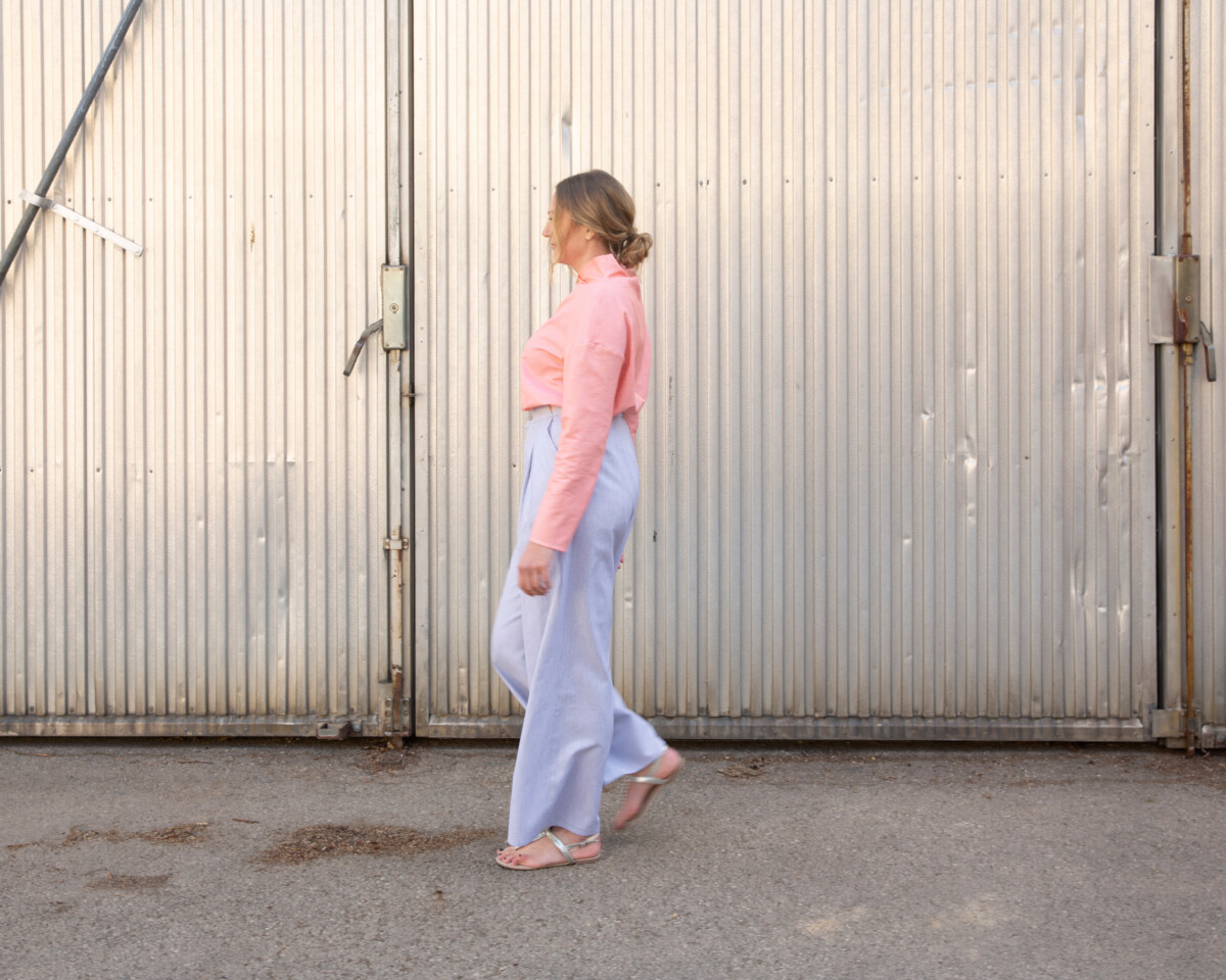 ever & anon, eine Frau im Profil vor industriellem Background in lockerer hellblauer Hose und einer rosa Bluse, Womenswear