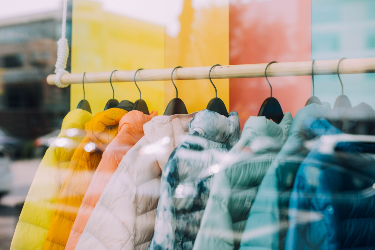 Pastellfarbene Jacken hängen nebeneinander in einem Schaufenster