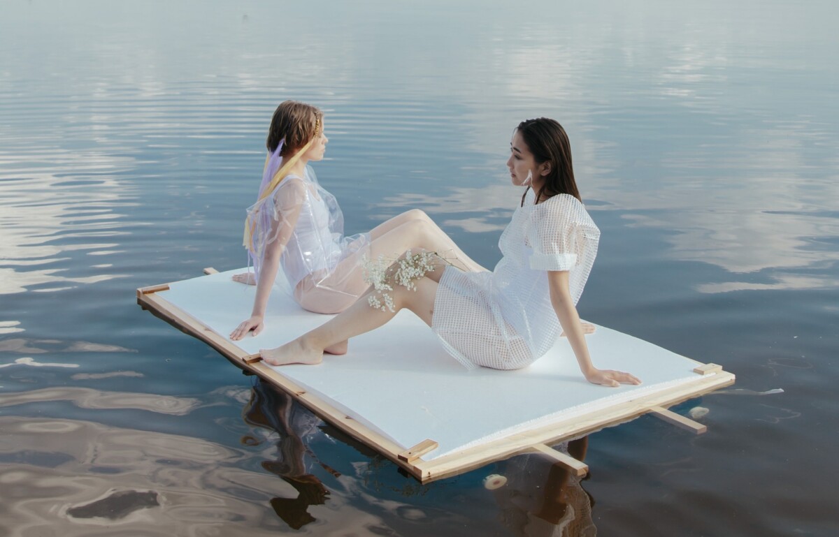 Zwei Personen sitzen auf einem großen Stück Holz im klaren Wasser
