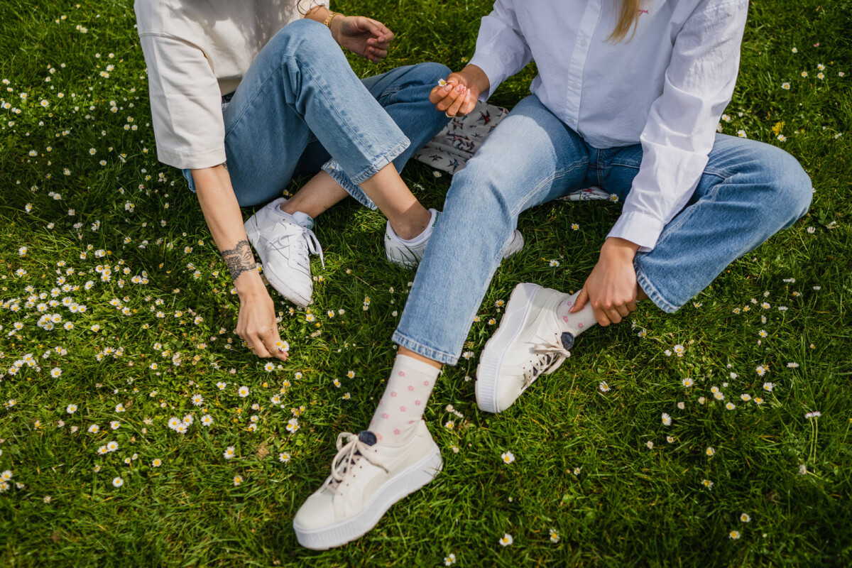 FUTURE:PEOPLE Zwei Personen sitzen in Jeans, weißem Shirt und weißen Sneakers auf einer Wiese, Womenswear