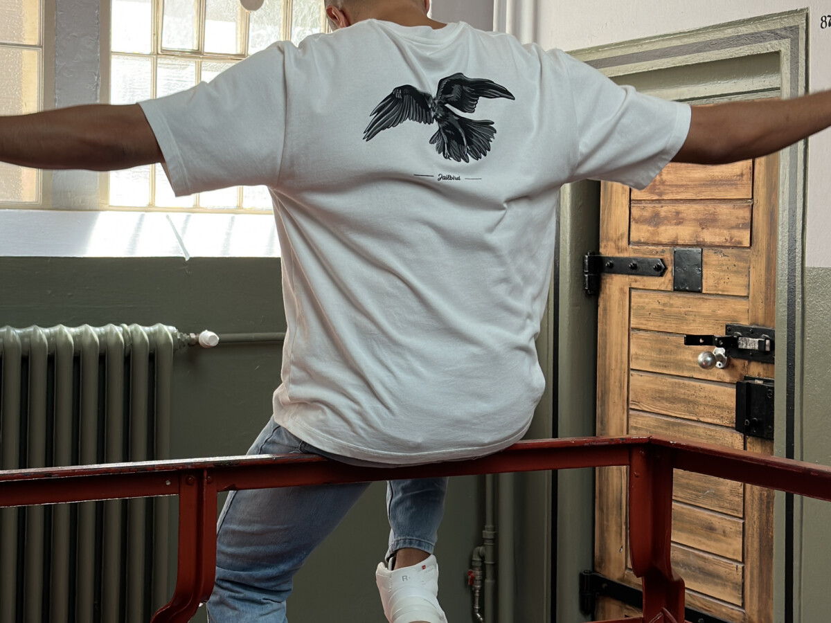 Streelated, ein Mann von hinten auf einem Geländer sitzend, dabei trägt er ein weißes Tshirt mit Aufrduck, Menswear.