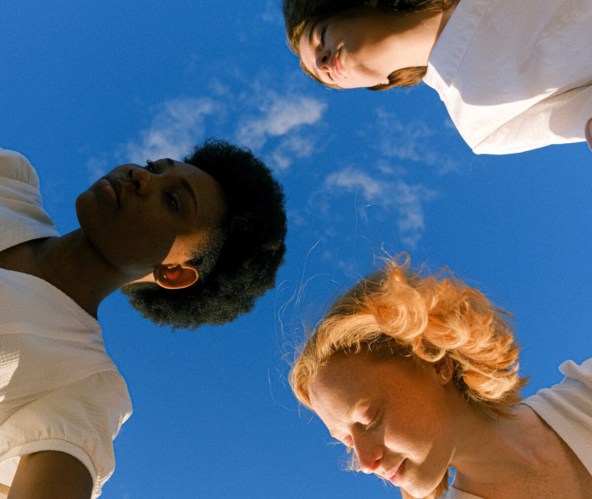 Titelbild existenzsichernde Löhne: Drei Gesichter, darüber ein knallblauer Himmel