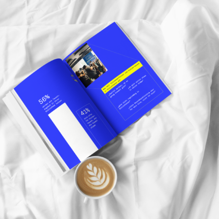 E-Book Kleidertausch neu denken Aufgeschlagenes Buch mit blauen Seiten liegt auf weißer Decke. Daneben ist ein Kaffeebecher zu sehen.